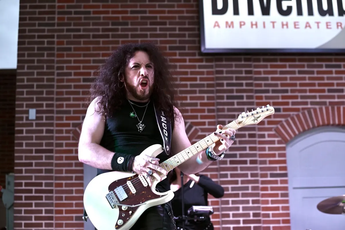 The guitarist mid-solo outside a brick amphitheater wall