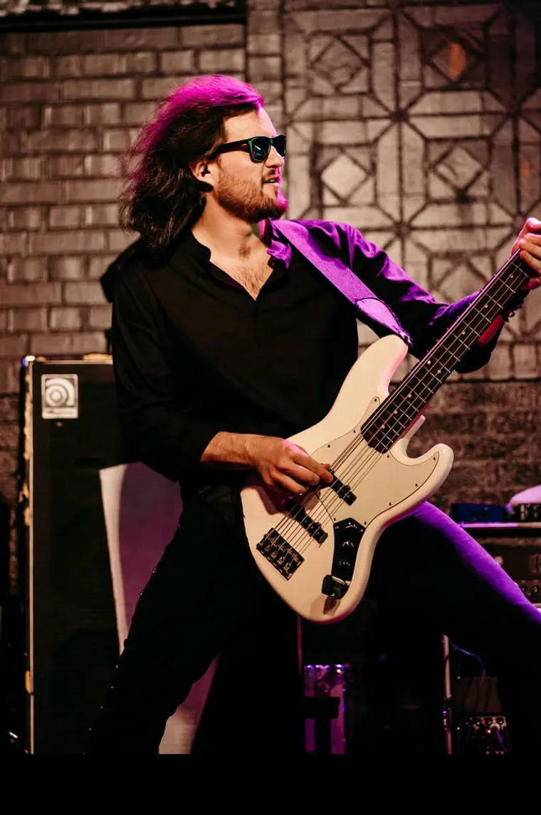 Jeff Smith in sunglasses playing a white jazz bass in front of an Ampeg cabinet